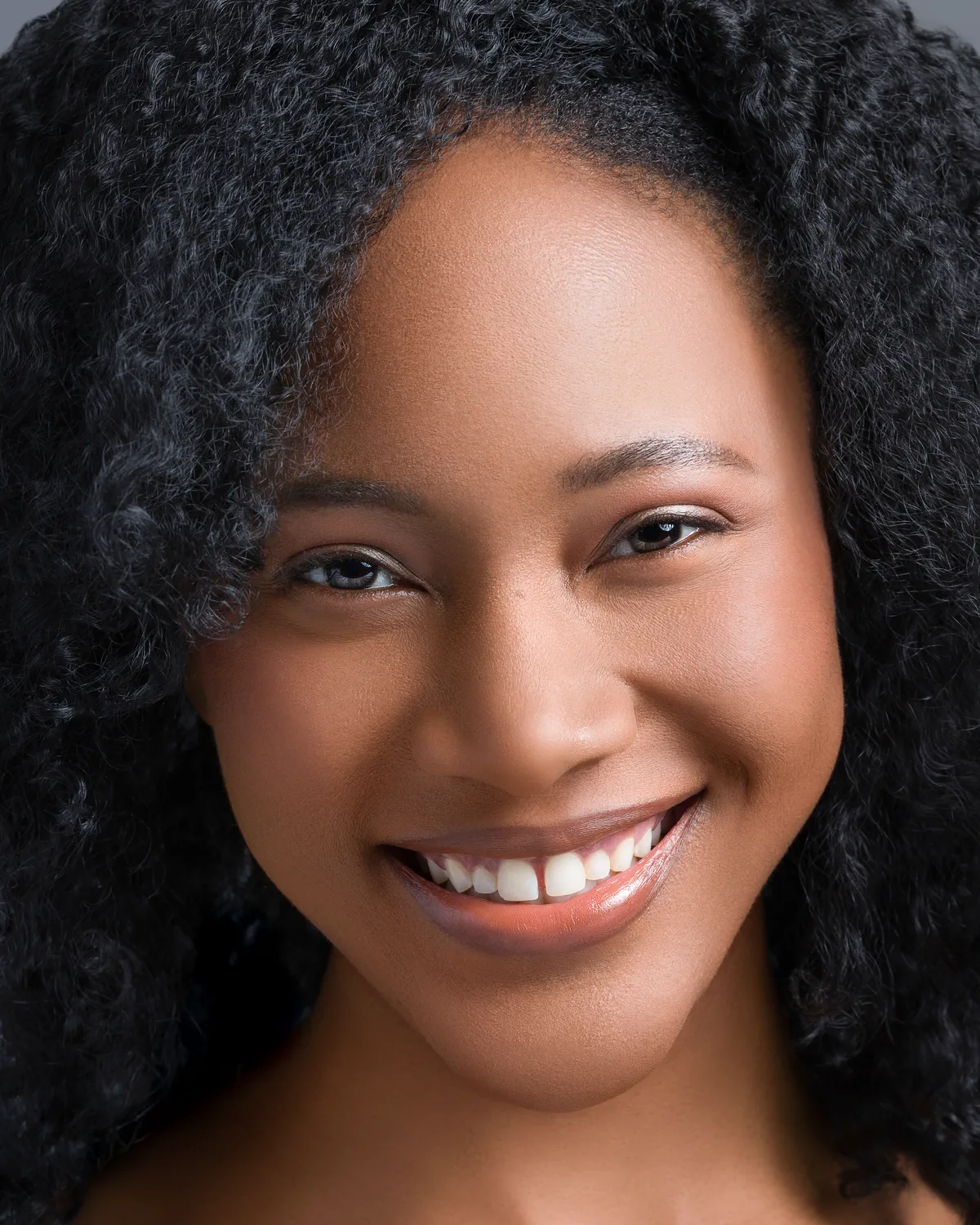 Close headshot of Ahdis Beruk smiling, hair down, against a grey background